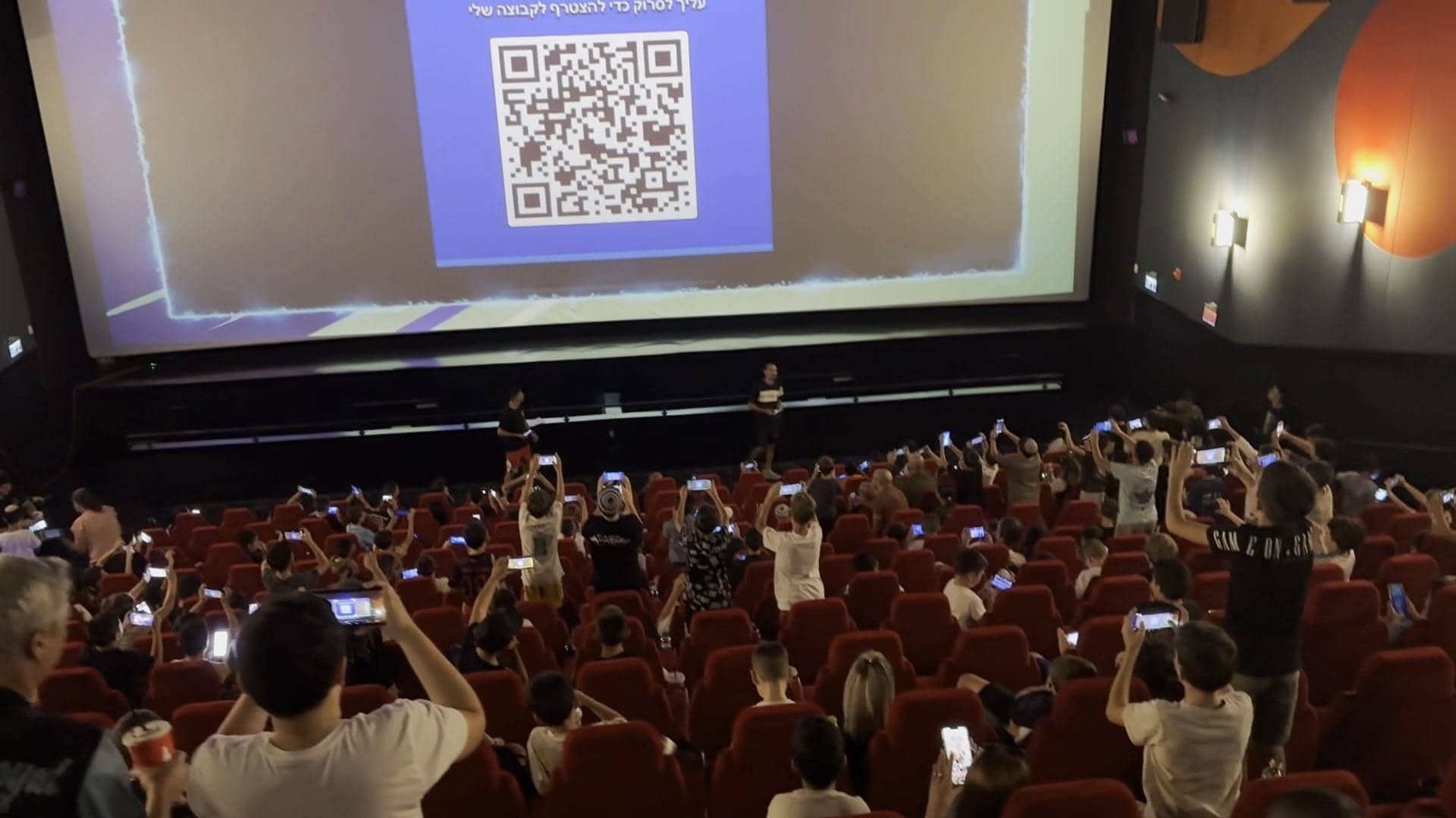 A full cinema audience holding up their phones to scan a code on the big screen